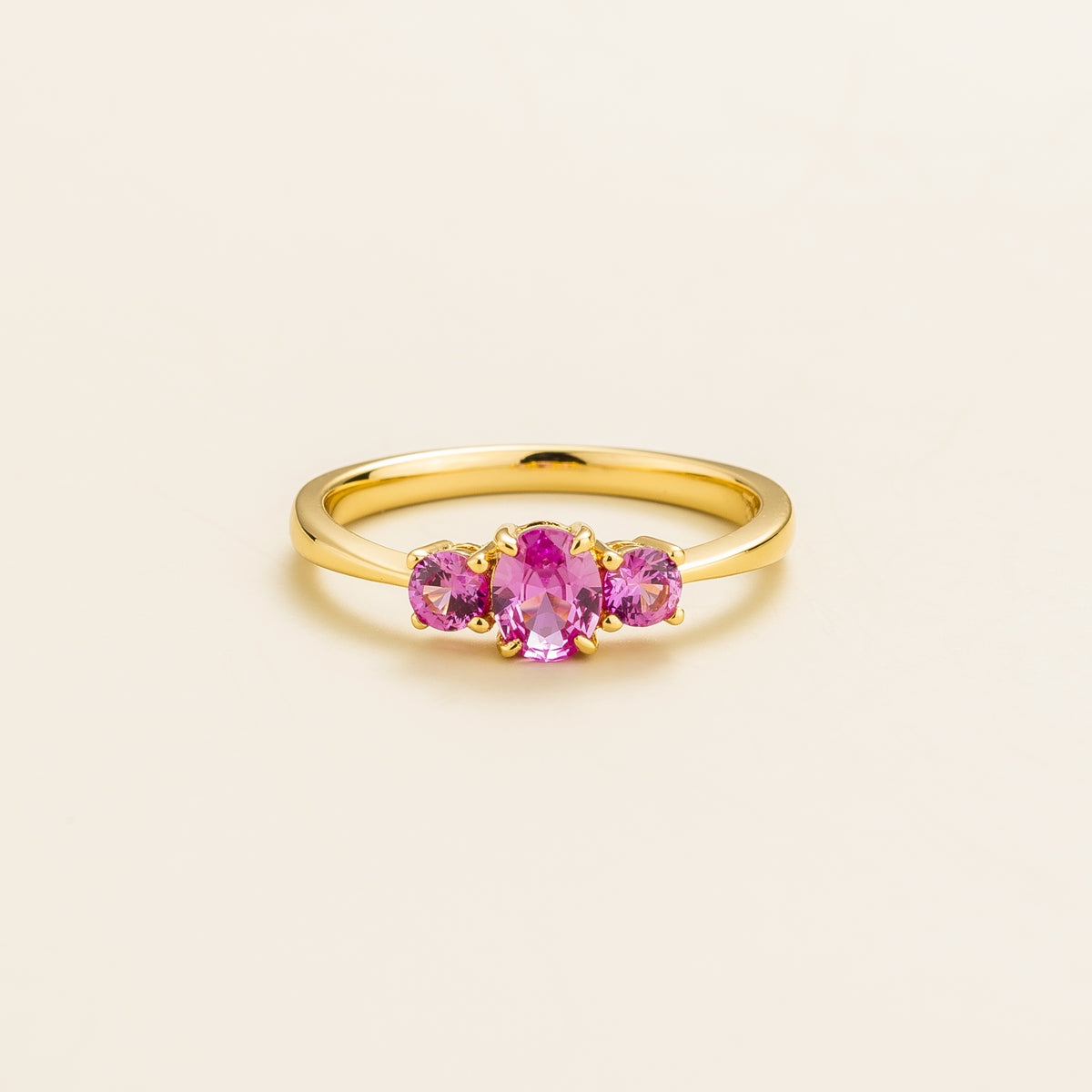A gold ring with three pink sapphire gemstones arranged in a row, displayed against a white background.