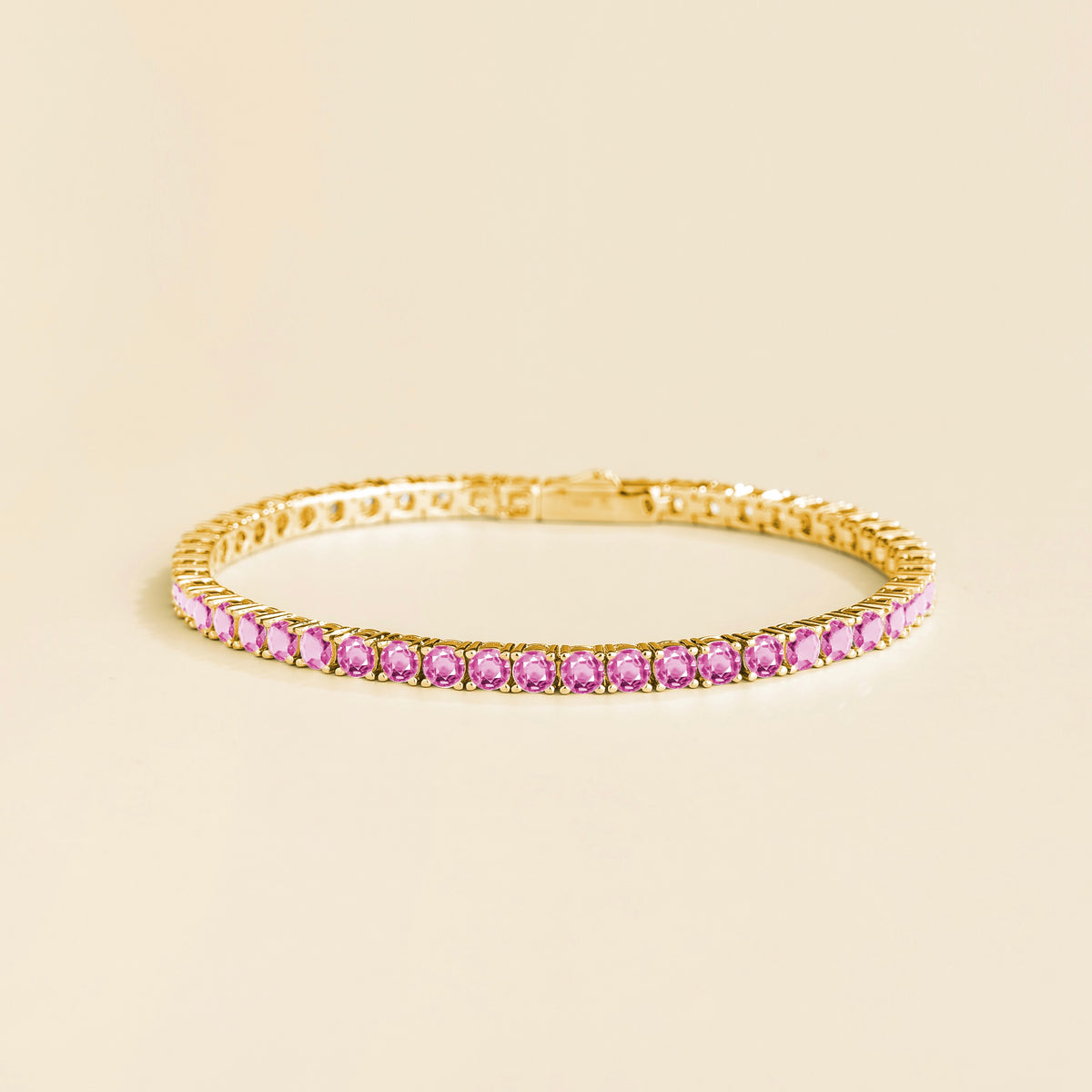 A gold tennis bracelet set with round pink sapphire gemstones on a plain background.
