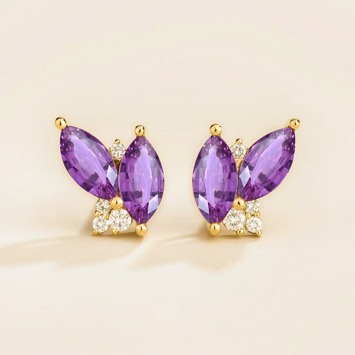 A pair of gold earrings featuring marquis purple sapphires and small round diamonds, with a butterfly-like shape.