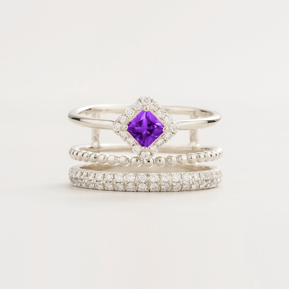 Amici triple-band stacking ring in white gold, princess-cut lab-grown purple sapphire in a diamond halo with beaded and pavé bands, front view | Juvetti London