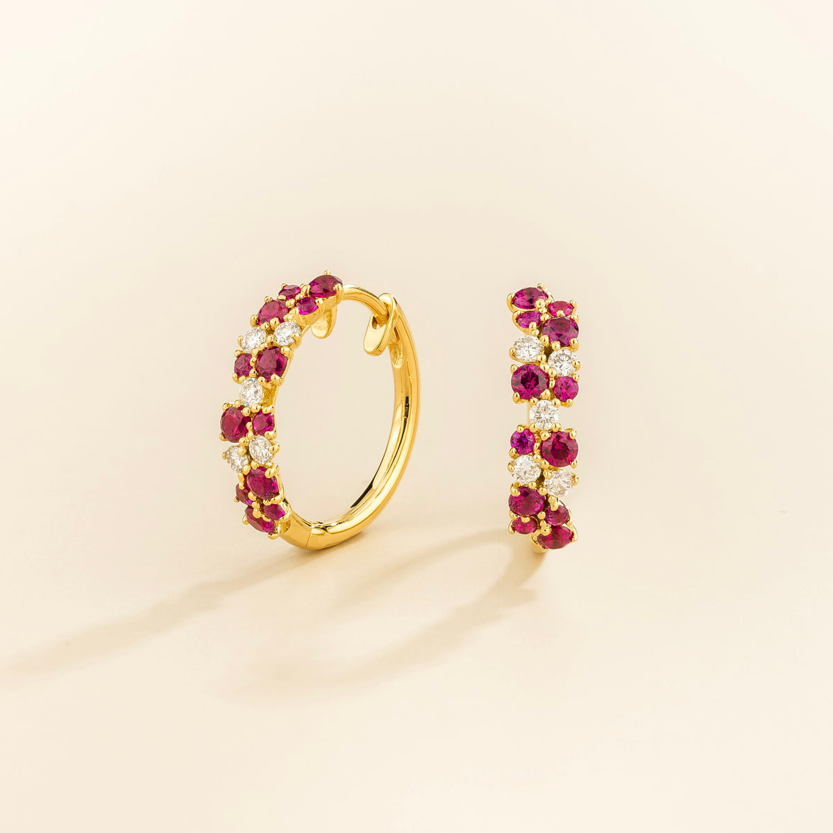 A pair of yellow gold huggie earrings set with cluster of round ruby and diamond accents, displayed against a neutral background.