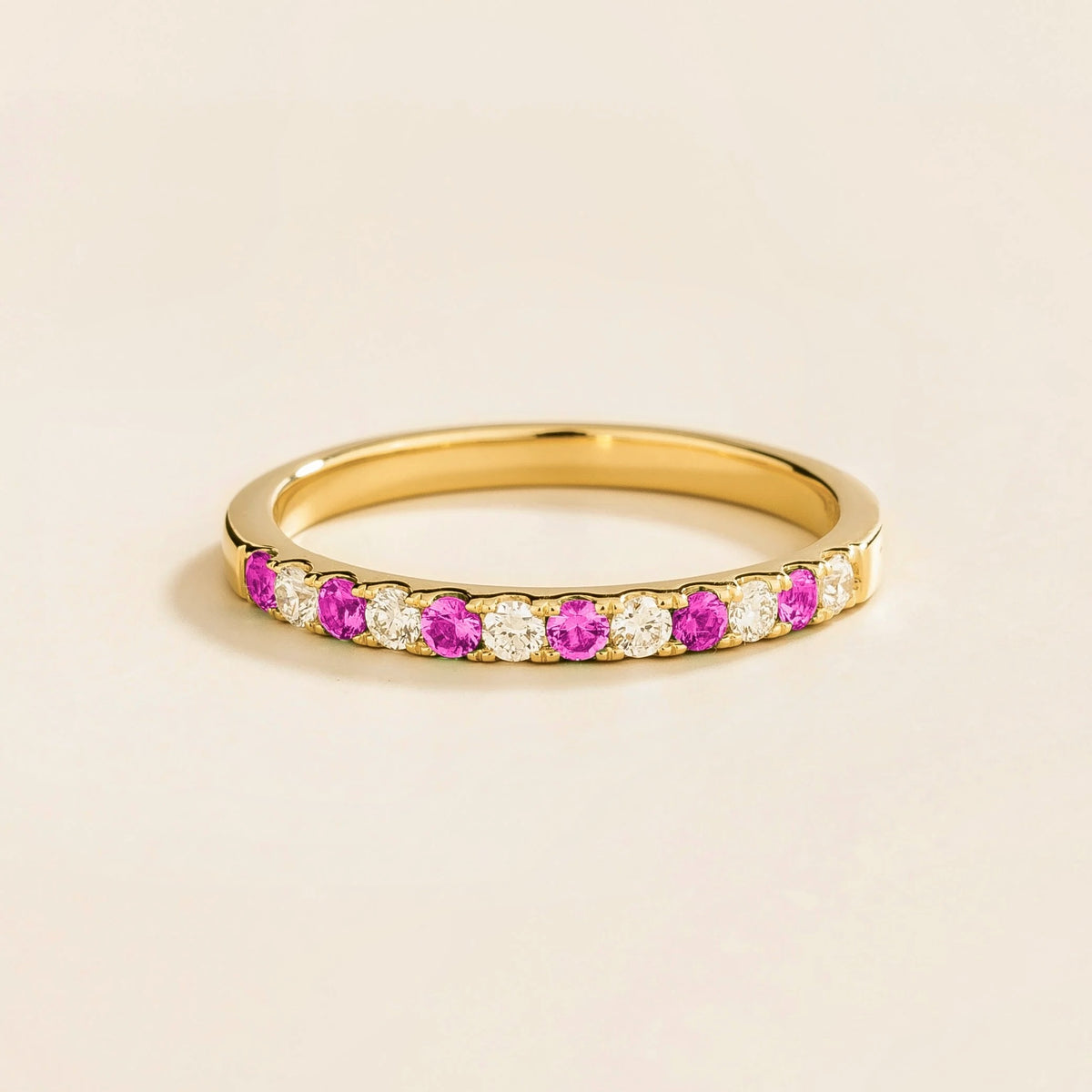 A gold ring with alternating vivid pink sapphire and diamond gemstones, forming a half eternity band design.
