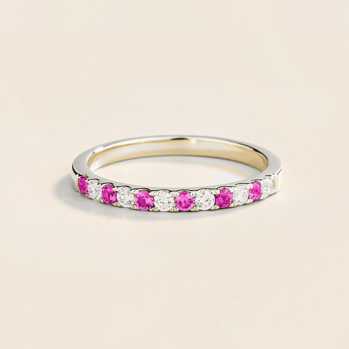 A white gold ring with alternating vivid pink sapphire and diamond elements, creating a half eternity band design.