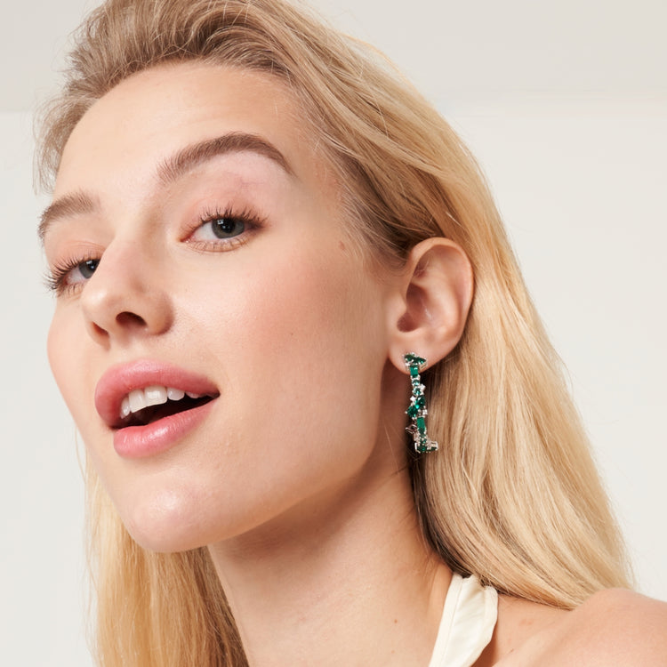 A model wearing Lanna large hoop earrings set with lab grown diamond and emerald gem stones.