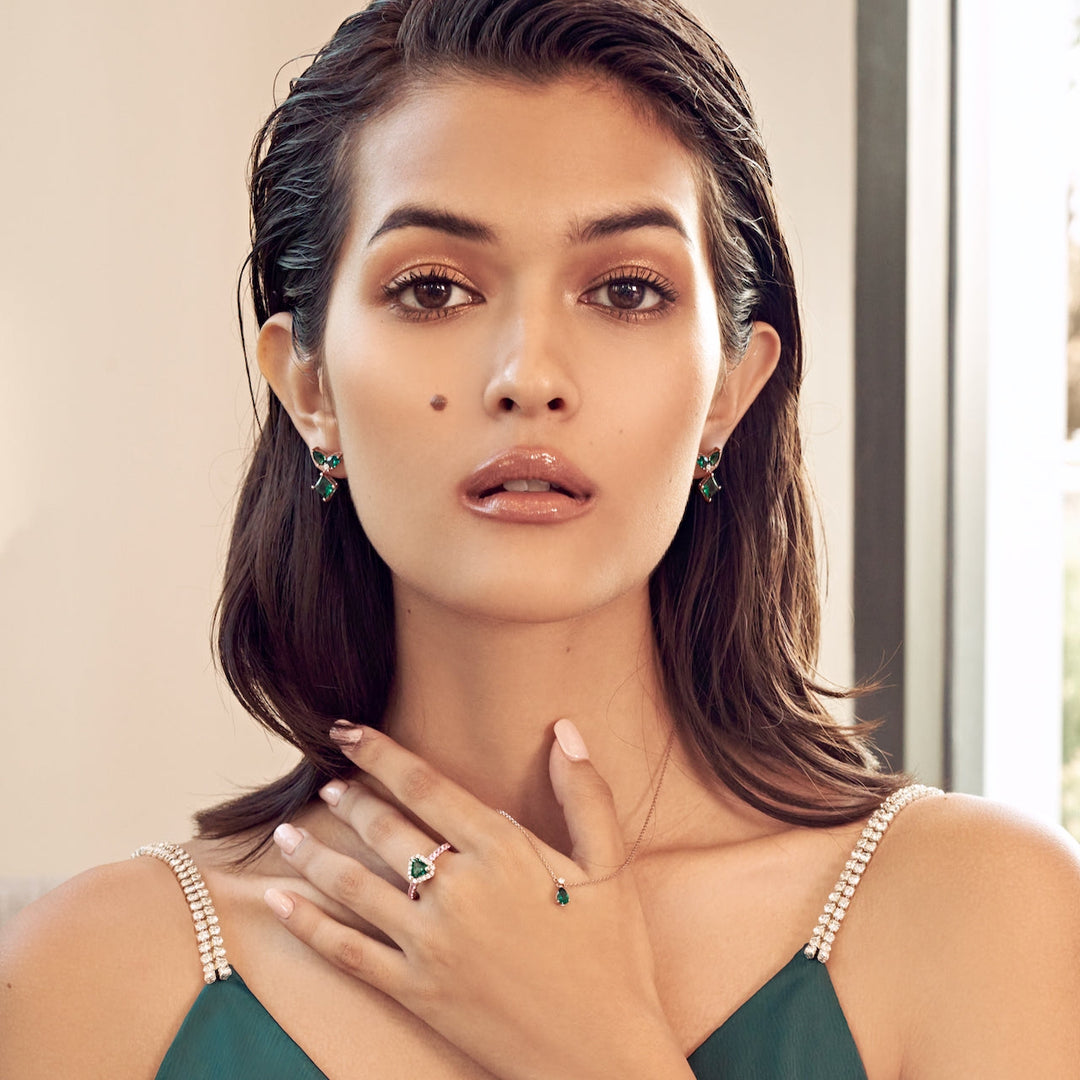 The model is wearing pear drop Ori necklace, triangle Melba ring and drop Amore earrings. The pieces are set with lab grown emerald, diamond and pink sapphire gem stones.